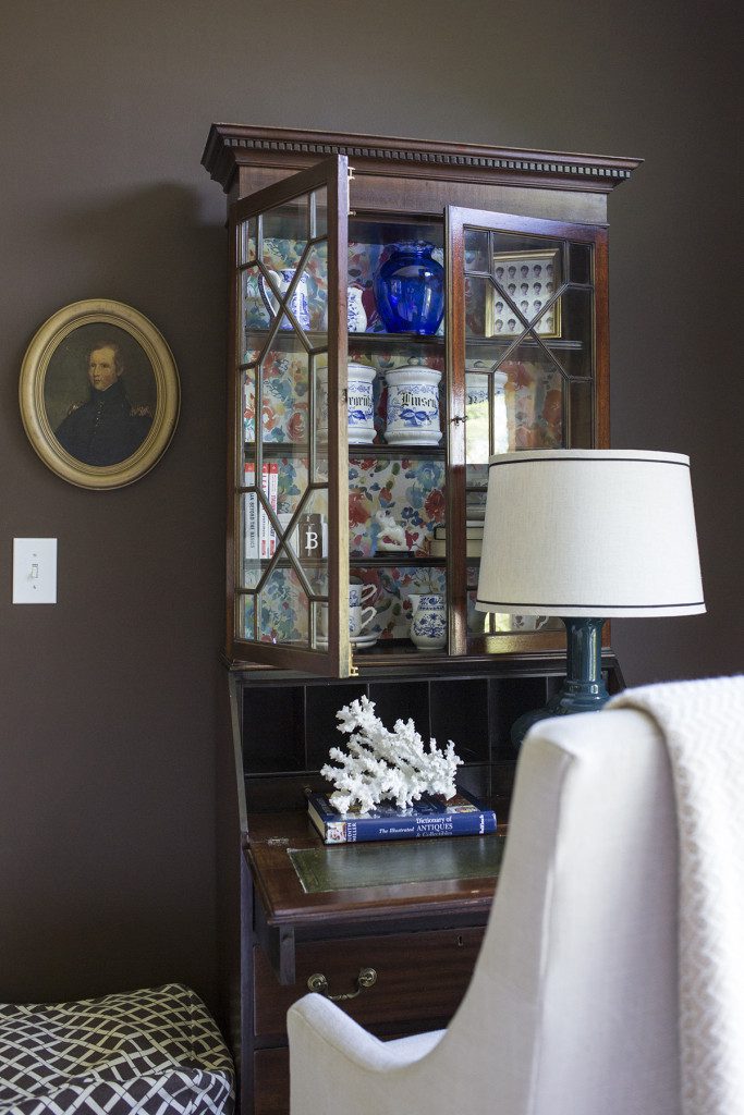 A living room with a table and chair, lamp, picture and china cabinet.