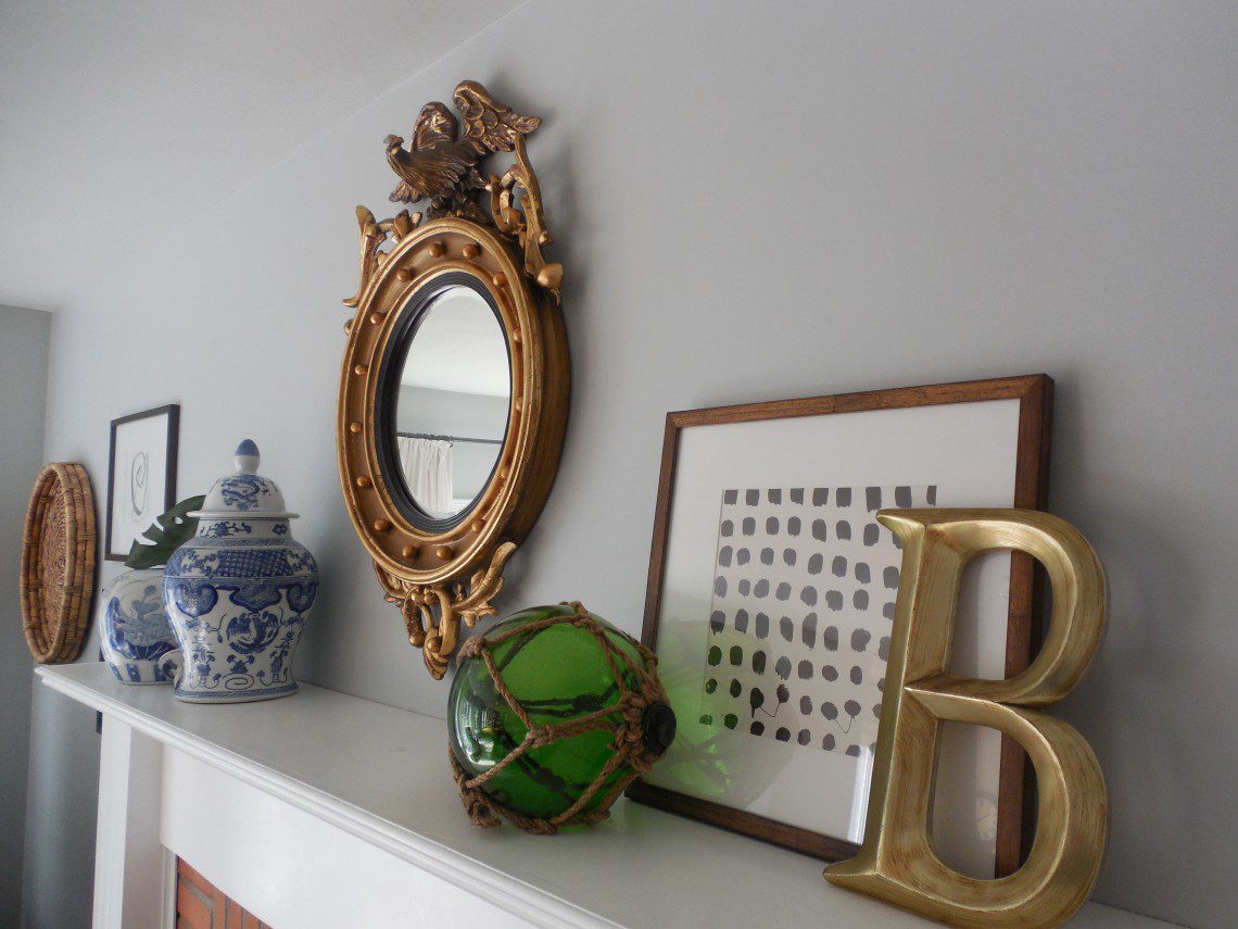 A mirror, vase and other objects are on the mantle.