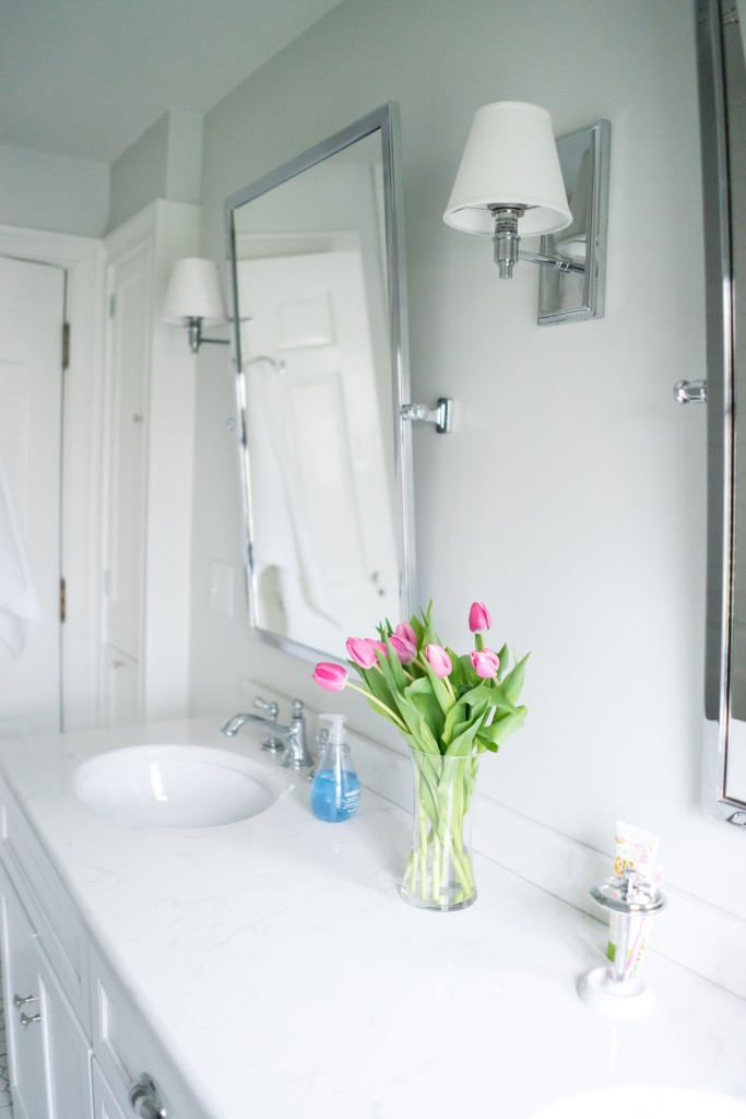 A bathroom with a sink, mirror and flowers in the vase.