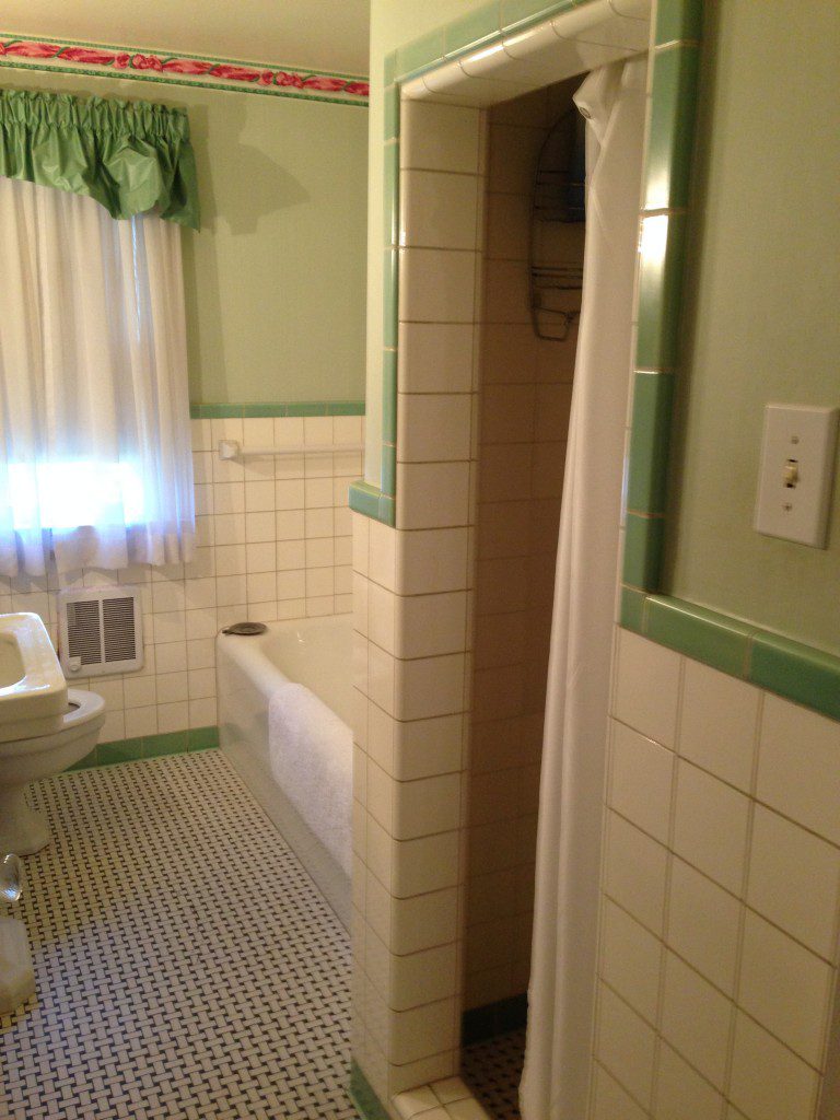 A bathroom with green and white tile, sink and tub.