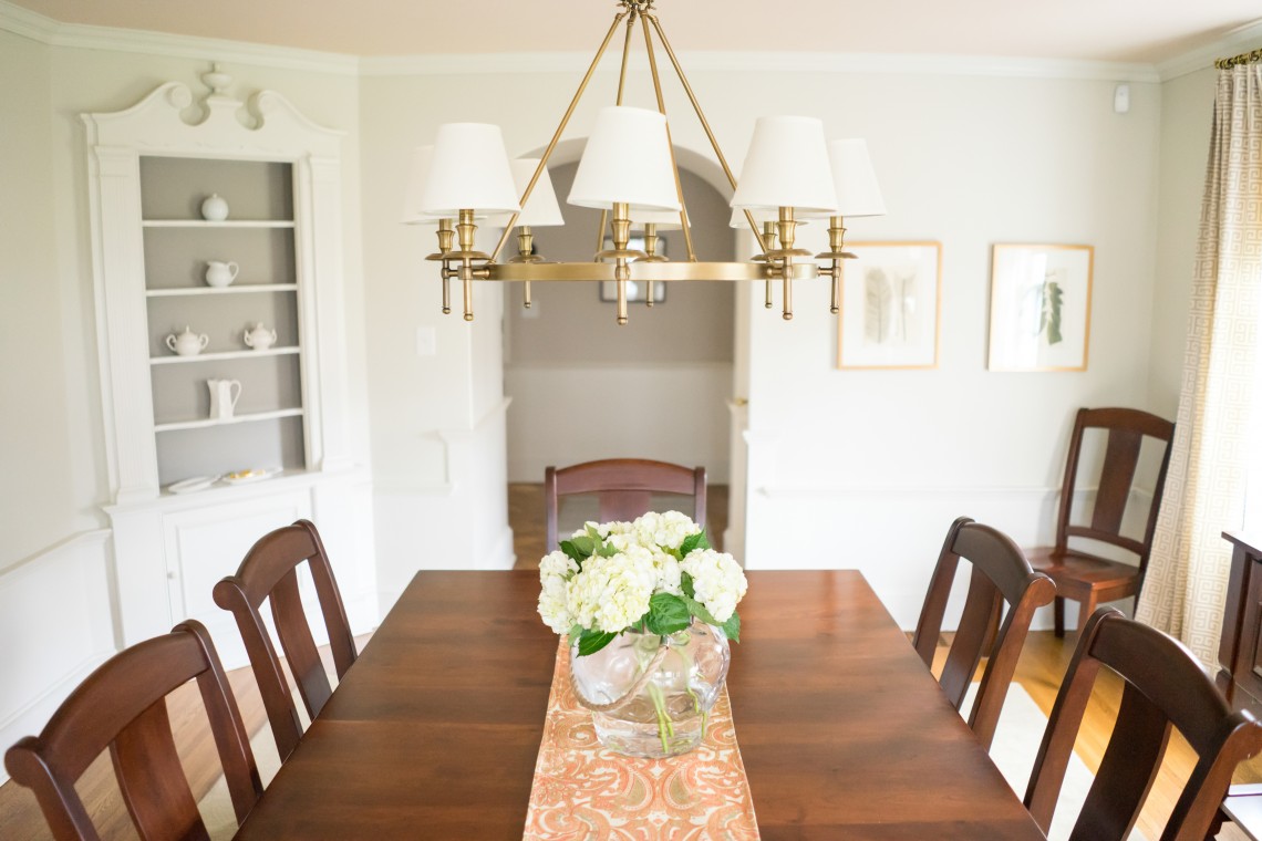 A dining room table with chairs and flowers in the center.