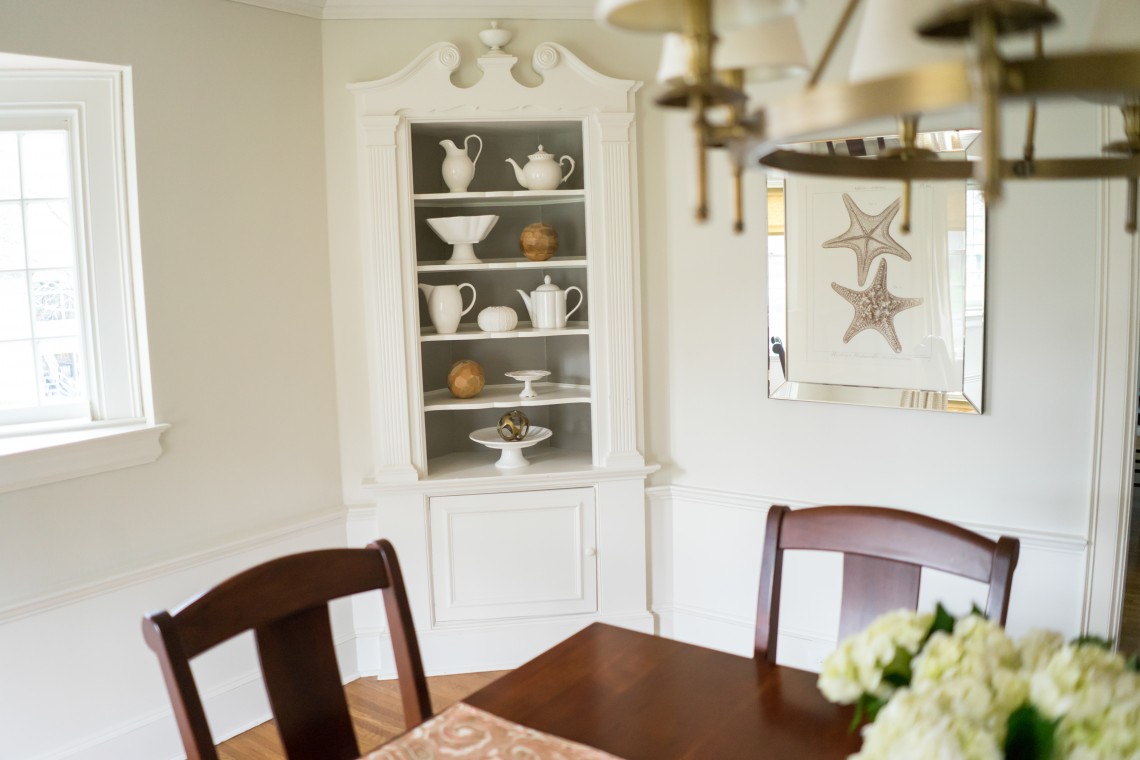 A dining room with a table and chairs, a mirror and a corner cabinet.