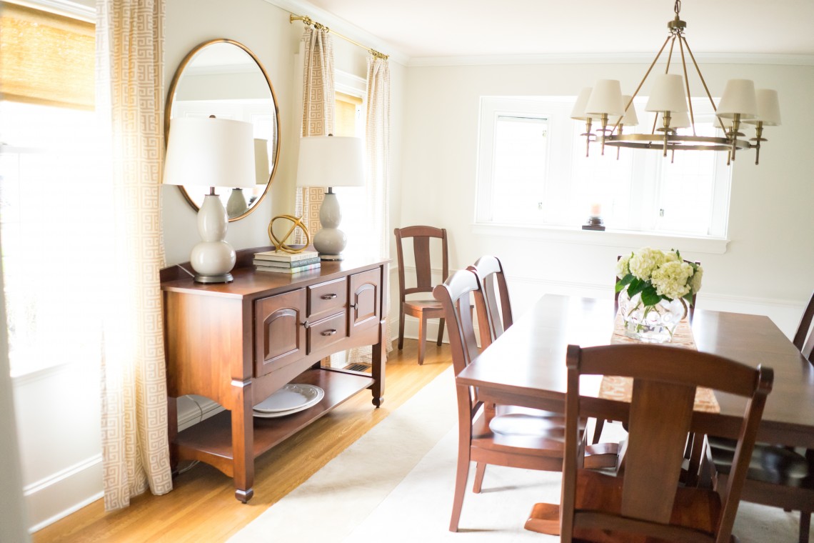 A dining room with a table and chairs, a mirror and a window.