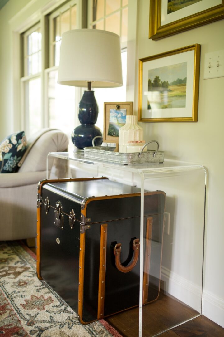 A black trunk is under a clear console table.