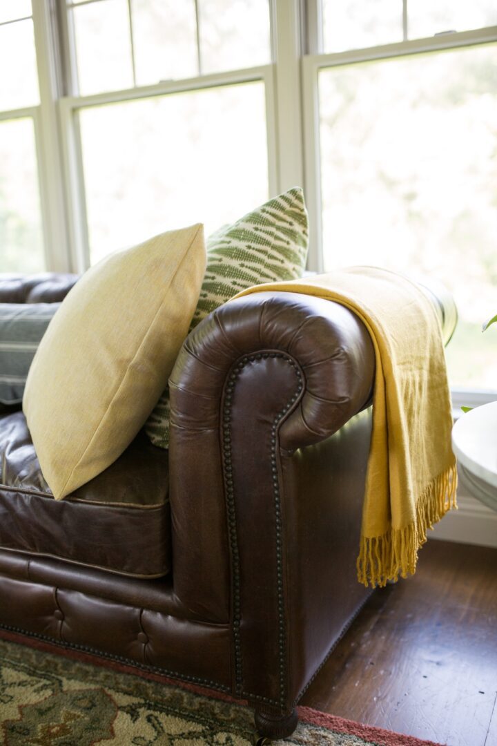 A brown leather couch with pillows and blankets on it.