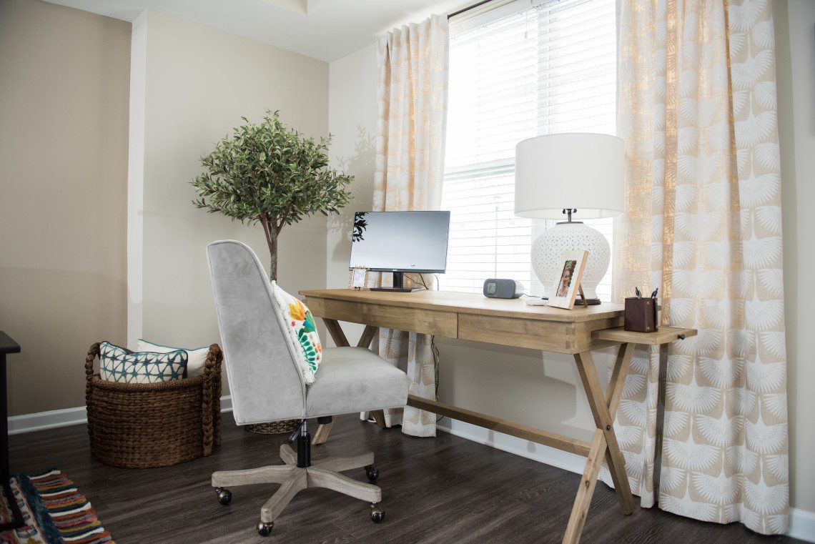 A desk with a chair and lamp in front of a window.