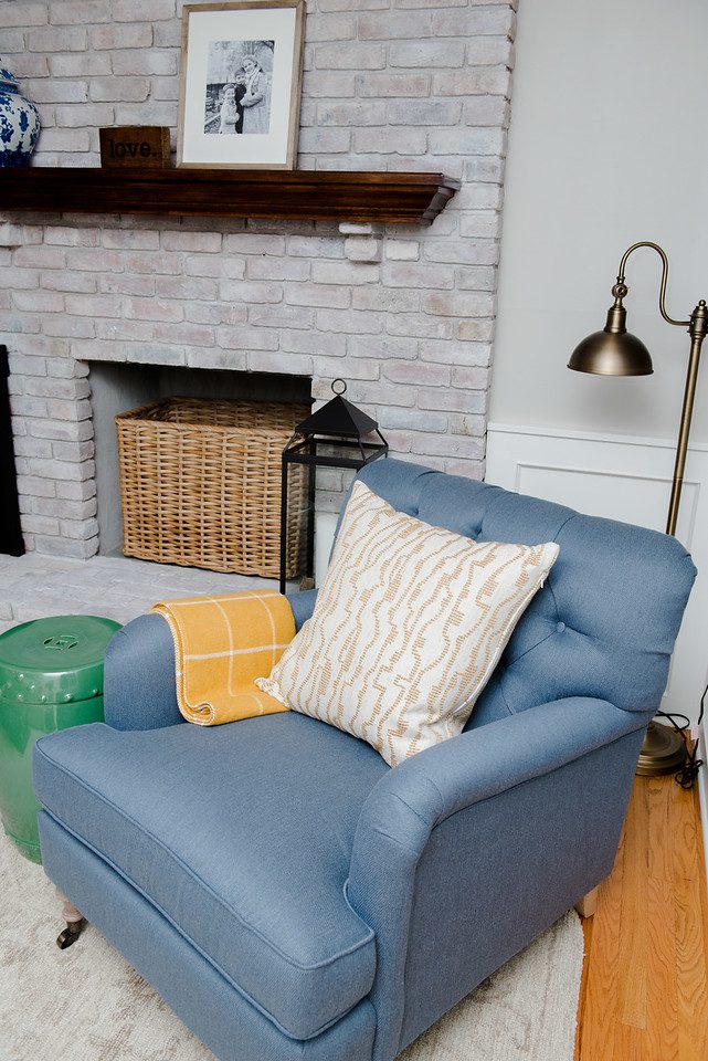 A blue chair with pillows and a lamp in front of the fireplace.