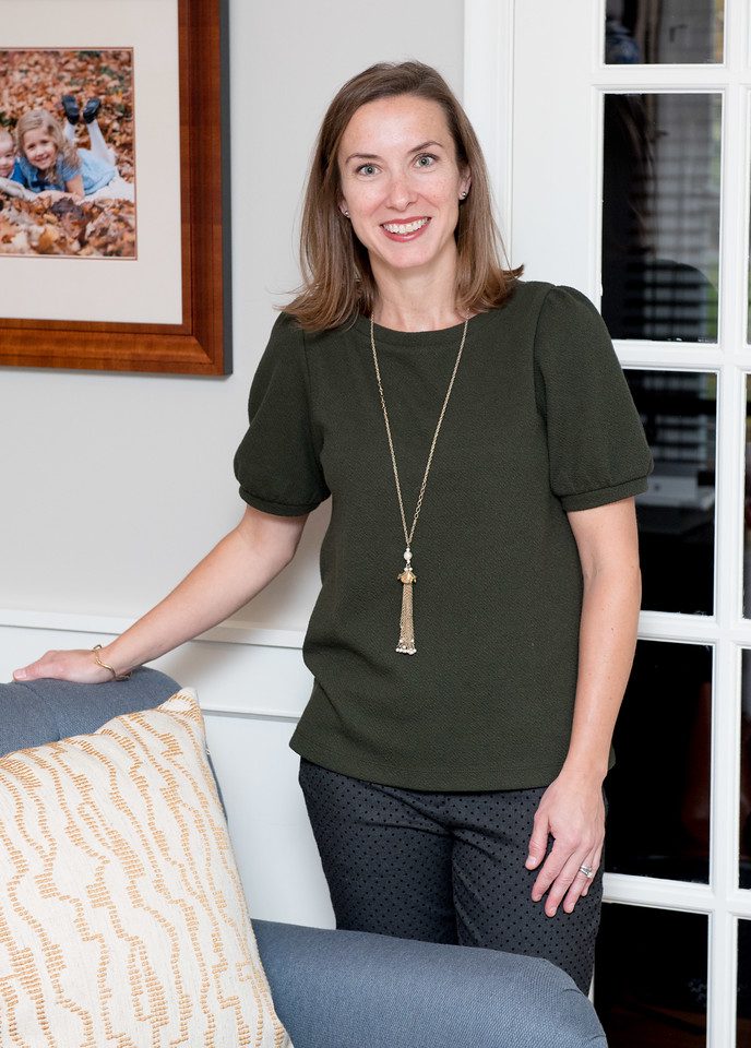 A woman standing in front of a chair wearing a necklace.